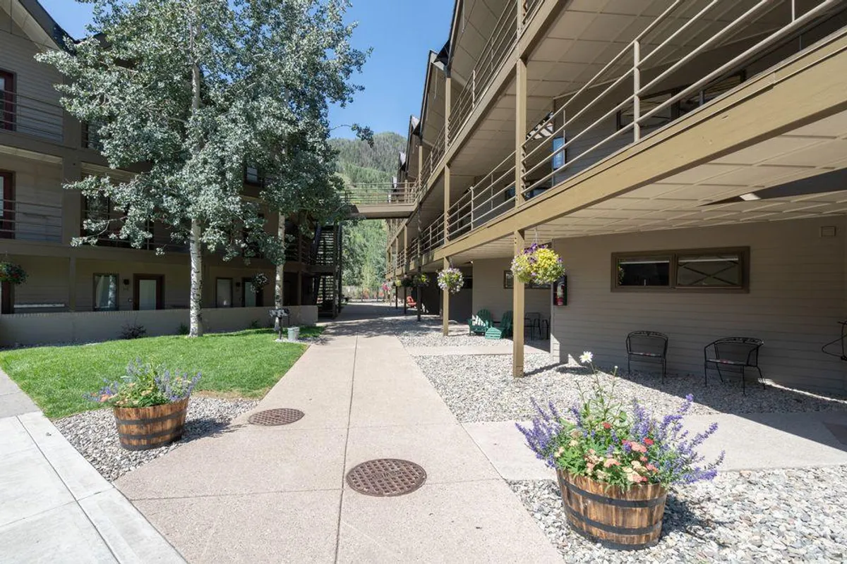 This image displays the inviting exterior of the property, with vibrant flower pots, a winding pathway, and lush greenery framing the building's architecture. The scene suggests a tranquil and welcoming environment perfect for relaxing or spending time outdoors with family.