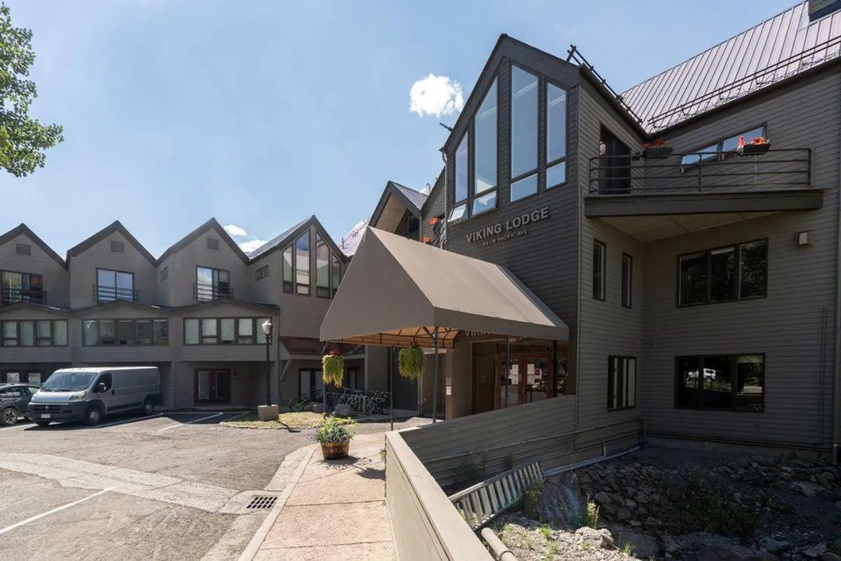 The entrance to Viking Lodge features a welcoming awning, large windows, and blooming outdoor planters. The sign marks the property, while the inviting entryway hints at both relaxation and readiness to explore the outdoors.