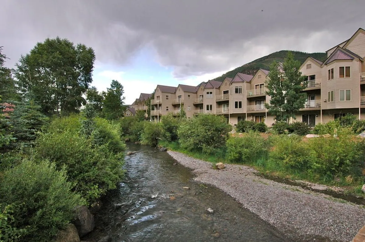 This image highlights a serene stream running alongside the buildings of the property, surrounded by lush greenery. The peaceful atmosphere is emphasized by the calm water and the inviting look of the nearby balconies, suggesting an ideal setting for relaxing and enjoying nature.